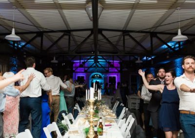 A reception at a wedding where people are line danceing arond a table.